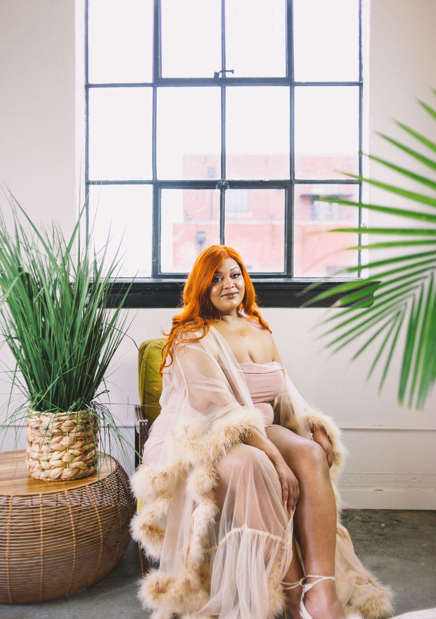 J. Woods seated in a blush-pink robe beside a tall window